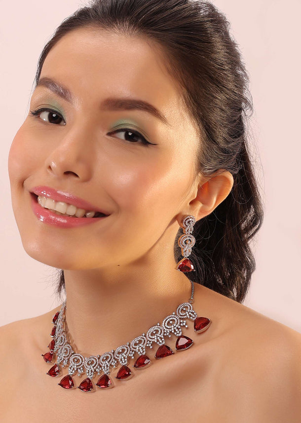 Silver Necklace With White Stones Infused In An Intricate Design Attached With Dangling Red Stones.