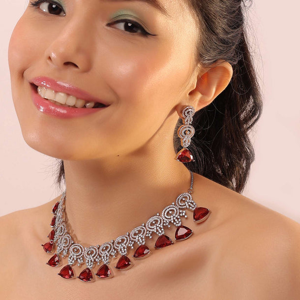 Silver Necklace With White Stones Infused In An Intricate Design Attached With Dangling Red Stones.